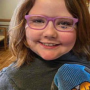 Mckenzie joined the competition — help win amazing prizes! child, smiling, glasses, light_brown_hair, indoor, shirt, graphic_tshirt, headphones, skull_graphic, reflective_sunglasses, purple_glasses, happy, portrait, person, casual_clothing, seated, wooden_floor, background_blur, young, closeup