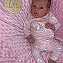 baby, infant, pink_blanket, wooden_sign, pajamas, bunny_pattern, soft_texture, milestone, lying_down, cute, newborn, face, person, socks, cozy, indoors, portrait, child, sleepwear, expressive_eyes