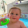 Elliot is registered to the contest to win money with this photo: baby, child, pool, water, toy, green, hand, face, skin, outdoor, sunlight, window, brick_wall, play, summer, cute, cheeks, splash, colorful, happy