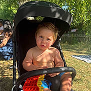 Elliot joined the competition — help win amazing prizes! toddler, child, stroller, outdoor, sunlight, toy, pop_it, shirtless, grass, tree, summer, play, baby, nature, park, people, shade, feet, expression, casual