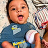 Raivy Alexander is registered to the contest to win money with this photo: baby, child, face, smiling, baseball, baseball_glove, hand, blue_sweater, patterned_bedspread, happy, lying_down, close_up, indoor, person, cute, playful, young_child, expression, toy, sports_equipment