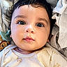 baby, infant, face, eyes, curly_hair, blanket, clothing, onesie, cute, portrait, closeup, child, soft_texture, indoors, resting, expression, adorable, skin, light, young