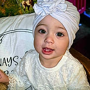 Amara joined the competition — help win amazing prizes! baby, child, headwrap, white_clothing, lace, smiling, face, eyes, indoor, pillow, text_on_pillow, toy, furniture, portrait, cute, young_child, sitting, decor, expression, closeup