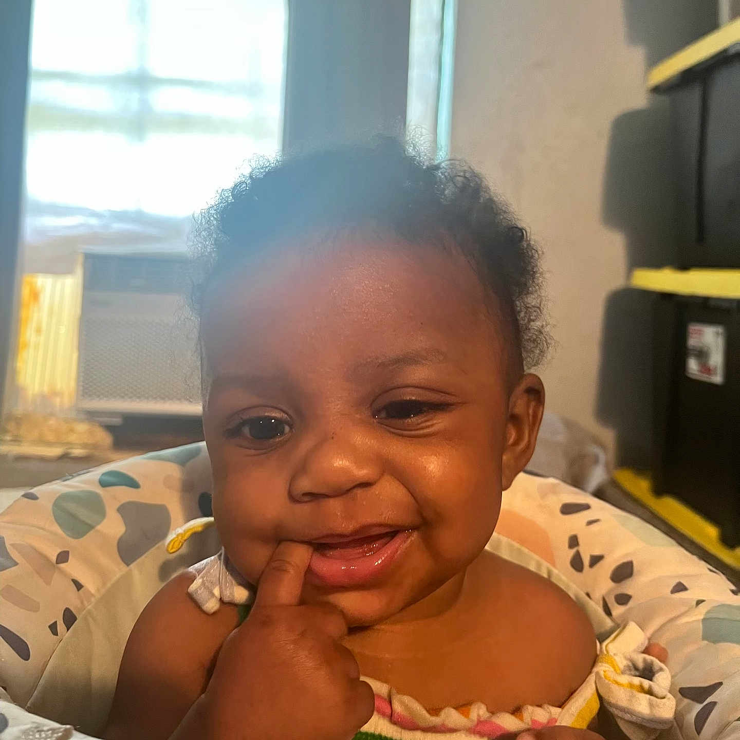 Kaliyah is registered to the contest to win money with this photo: baby, child, colorful, curly_hair, cushion, expression, face, finger_in_mouth, furniture, happy, home, indoor, infant, light, person, portrait, seat, skin, smile, window