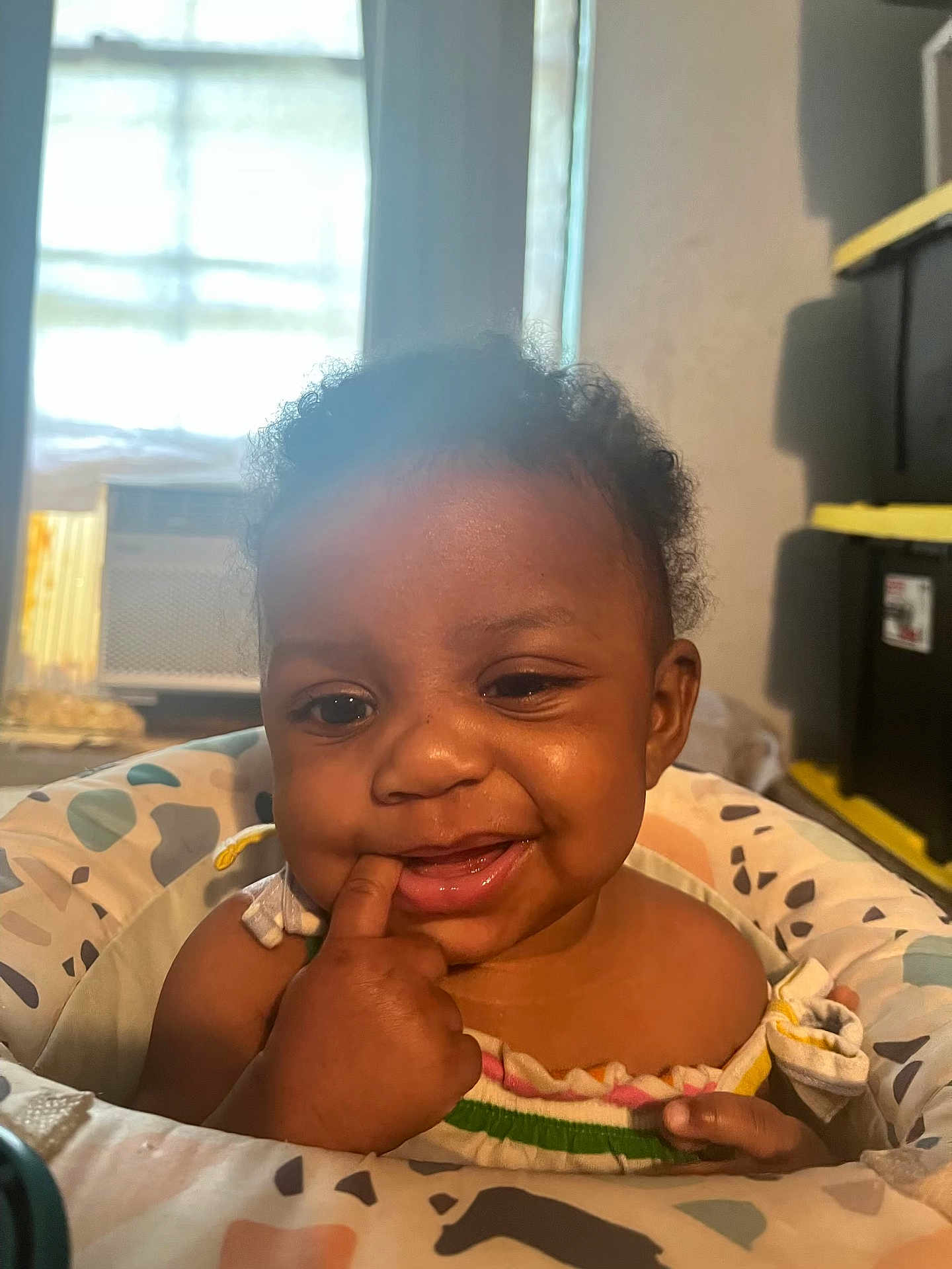 Kaliyah is registered to the contest to win money with this photo: baby, child, smile, finger_in_mouth, curly_hair, cushion, seat, indoor, window, light, skin, face, person, happy, expression, furniture, colorful, home, infant, portrait