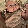 baby, infant, headband, flower, knitted_outfit, lying_down, pillow, floral_pattern, cute, person, child, skin, face, eyes, arm, hand, indoors, portrait, young, apparel