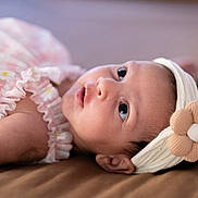 Heera is registered to the contest to win money with this photo: baby, infant, headband, flower, pink_dress, lying_down, close_up, cute, child, portrait, soft_lighting, indoors, skin, face, eyes, young_child, head, apparel, fabric, resting