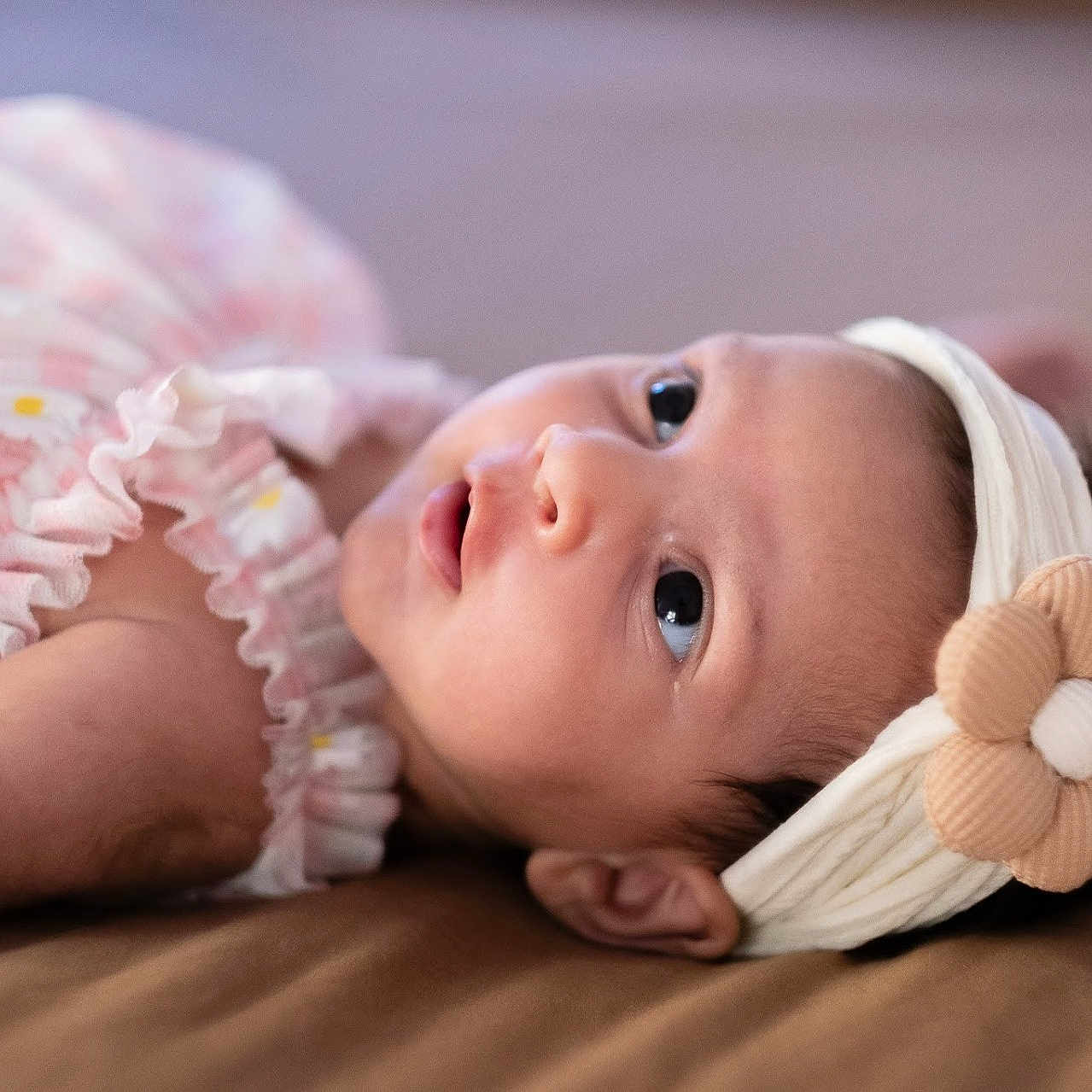 Heera is registered to the contest to win money with this photo: apparel, baby, child, close_up, cute, eyes, fabric, face, flower, head, headband, indoors, infant, lying_down, pink_dress, portrait, resting, skin, soft_lighting, young_child