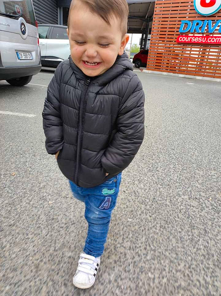 Maydën a rejoint le concours — aidez-le/la à gagner de superbes lots ! asphalt, automotive_tire, blond, car, child, denim, electric_blue, facial_expression, footwear, hairstyle, jeans, joy, person, plant, road_surface, sleeve, smile, tire, toddler, vehicle