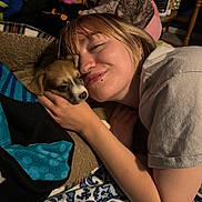 Moon is registered to the contest to win money with this photo: person, puppy, dog, bed, blanket, indoor, snuggling, face, piercing, plush_toys, comfort, cuddle, happy, resting, casual_clothing, young_adult, animal, warm, relaxation, home
