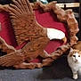 cat, orange_cat, white_cat, wooden_carving, eagle, sculpture, carpet, indoor, animal, pet, feline, decor, ornament, curious, floor, furniture, brown, red_background, texture, wildlife_replica