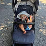 Theodore is registered to the contest to win money with this photo: baby, stroller, pacifier, hat, sunhat, outdoor, pavement, foot, child, blue_eyes, playful, shade, sunlight, seat, stripes, infant, baby_clothing, baby_seat, person, summer