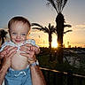 baby, child, smile, hands, sunset, palm_trees, blue_sky, outdoor, person, cute, happy, portrait, shorts, shirt, nature, sunlight, parking_lot, fence, adult, holding