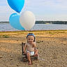 Theodore is registered to the contest to win money with this photo: baby, balloons, beach, sand, water, lake, child, cap, diaper, wooden_chair, outdoor, nature, sky, trees, playful, cute, summer, sunlight, smiling, sitting
