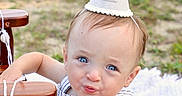 Theodore is registered to the contest to win money with this photo: baby, child, party_hat, outdoor, blue_eyes, striped_clothing, wooden_chair, grass, curious_expression, cute, first_birthday, infant, portrait, summer, one_year_old, celebration, hat, person, sitting, daylight
