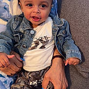 Ashad is registered to the contest to win money with this photo: adult_hand, blue_nail_polish, casual_clothing, child, close_up, couch, curly_hair, cute, denim_jacket, family, happy, holding, indoor, patterned_pants, person, portrait, seated, smiling, toddler, young_child