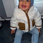 Maë participe au concours pour gagner de l'argent avec cette photo : toddler, child, smiling, blue_hat, fleece_jacket, jeans, sneakers, indoor, window, floor, happy, cute, baby, clothing, person, portrait, seated, casual, headwear, footwear