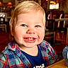 toddler, child, smile, plaid_shirt, blue_eyes, indoor, restaurant, table, wooden_table, watch, messy_face, happy, person, clothing, face, portrait, sitting, cute, baby, casual
