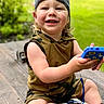 Cameron is registered to the contest to win money with this photo: toddler, child, smiling, cap, backward_cap, camouflage, outdoor, toy, phone, sitting, wooden_deck, greenery, happy, cute, person, summer, casual_clothing, shoes, play, portrait