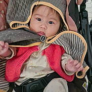 Nina participe au concours pour gagner de l'argent avec cette photo : baby, child, stroller, hood, cape, red_vest, pajamas, seatbelt, indoor, curious, face, hand, footwear, blanket, polka_dots, striped, fabric, infant, seated, cute