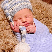 Kohen joined the competition — help win amazing prizes! newborn, baby, sleeping, knitted_hat, pom_pom, blue_wrap, blanket, soft_texture, cozy, infant, cute, peaceful, portrait, closeup, indoors, child, headwear, resting, warm, snuggled