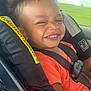 child, toddler, car_seat, smiling, orange_shirt, seatbelt, happy, face, hair, window, car_interior, safety, seat, travel, cute, expression, daylight, vehicle, young_child, portrait
