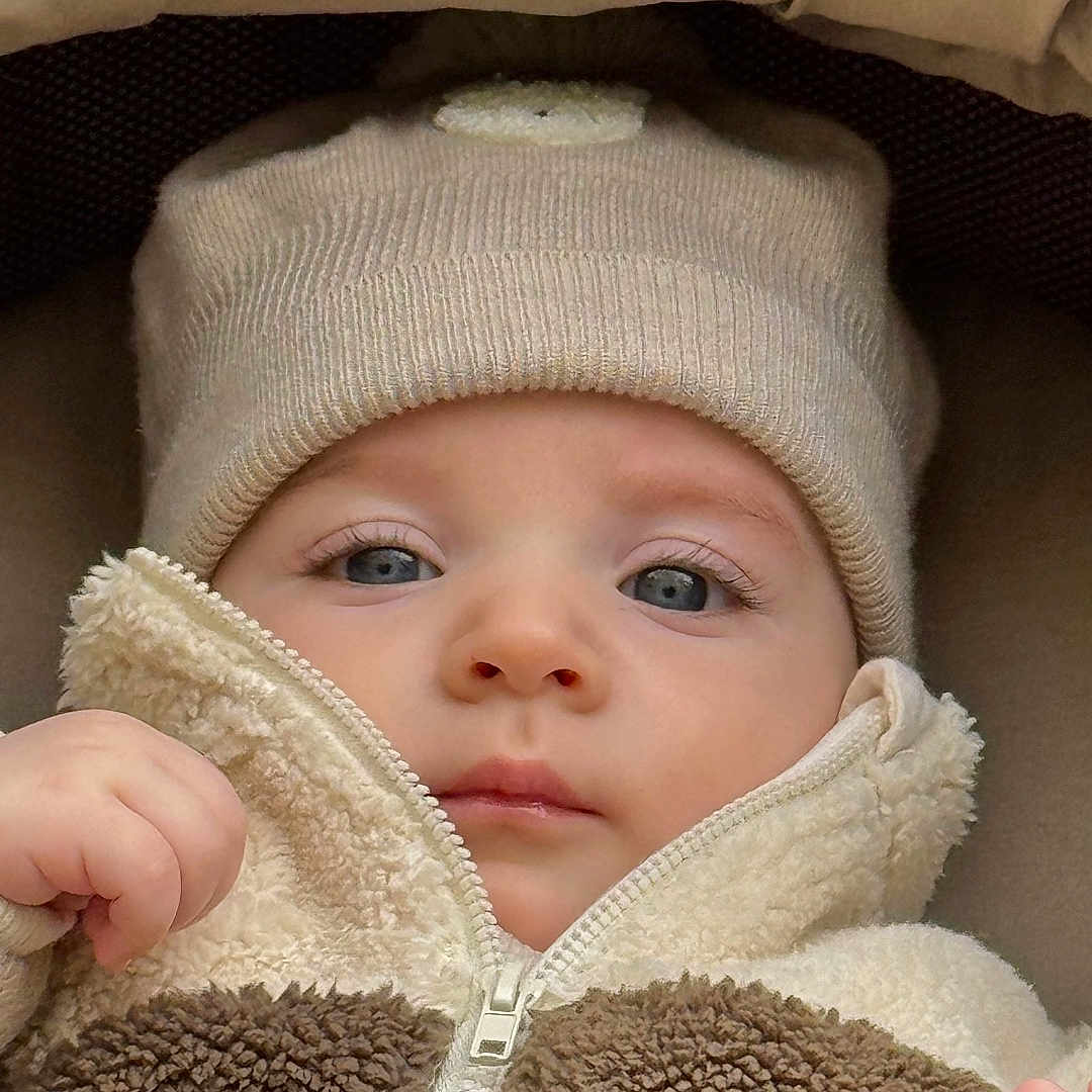 Edward participe au concours pour gagner de l'argent avec cette photo : baby, blue_eyes, brown, child, close_up, cream, cushion, cute, face, fleece, hand, hat, indoor, infant, jacket, knit_hat, portrait, soft_fabric, warm_clothing, zipper