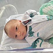 Rónán joined the competition — help win amazing prizes! newborn, baby, infant, hospital, bassinet, blanket, crocheted, onesie, dinosaur, clothing, face, head, sleeping, bed, person, cute, small, resting, indoor, peaceful