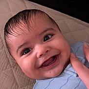 Ayden is registered to the contest to win money with this photo: baby, infant, child, smiling, laughing, portrait, face, eyes, open_mouth, teeth, blue_outfit, wet_hair, lying_down, bed, quilt, blanket, headboard, adult_hand, indoor, happy