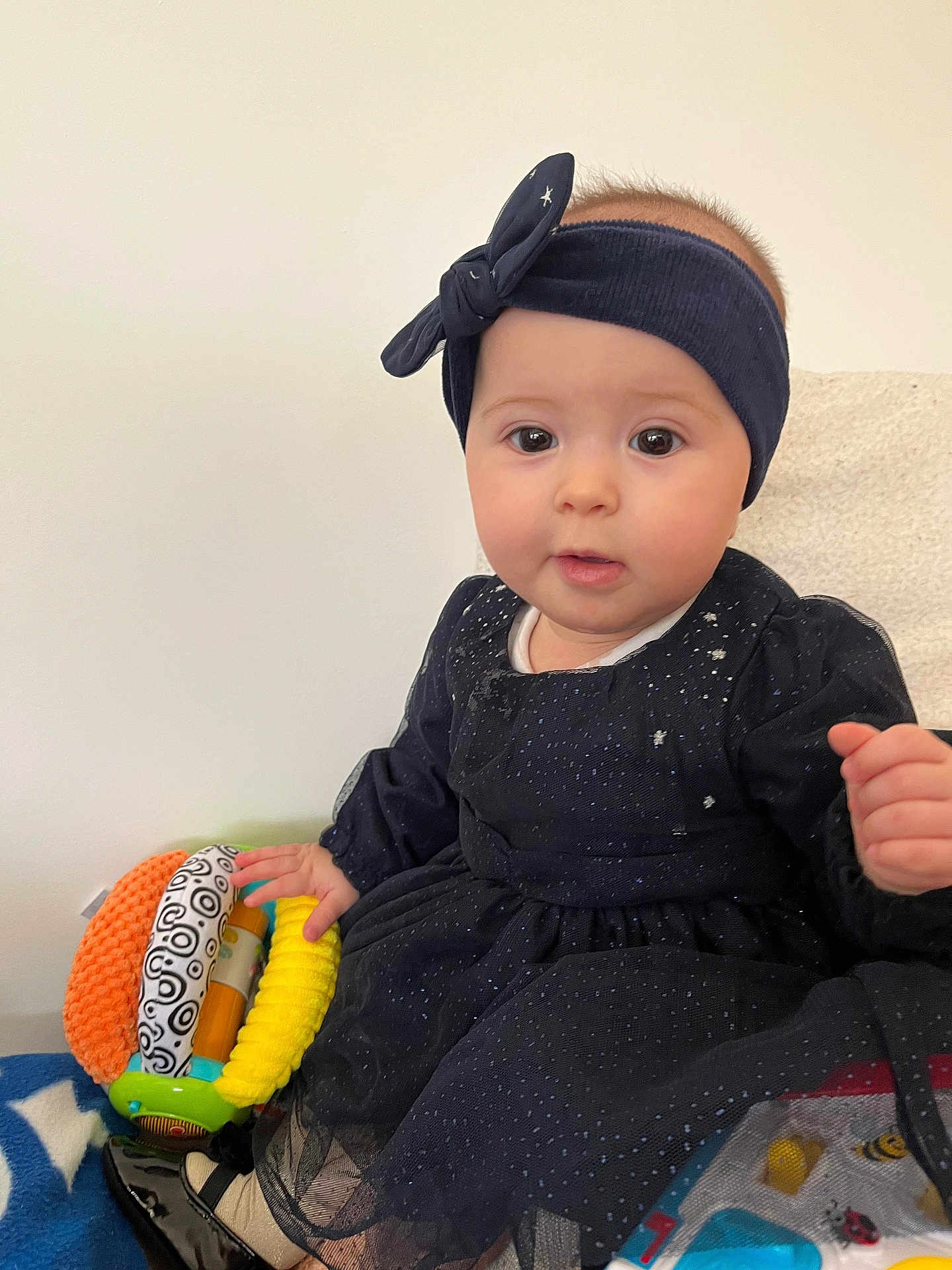 Luiza participe au concours pour gagner de l'argent avec cette photo : baby, infant, child, headband, rattle, dress, portrait, cute, big_eyes, face, hand, sitting, blank_wall, blanket, fabric, indoor, soft_toy, curious_expression, cheeks, skin