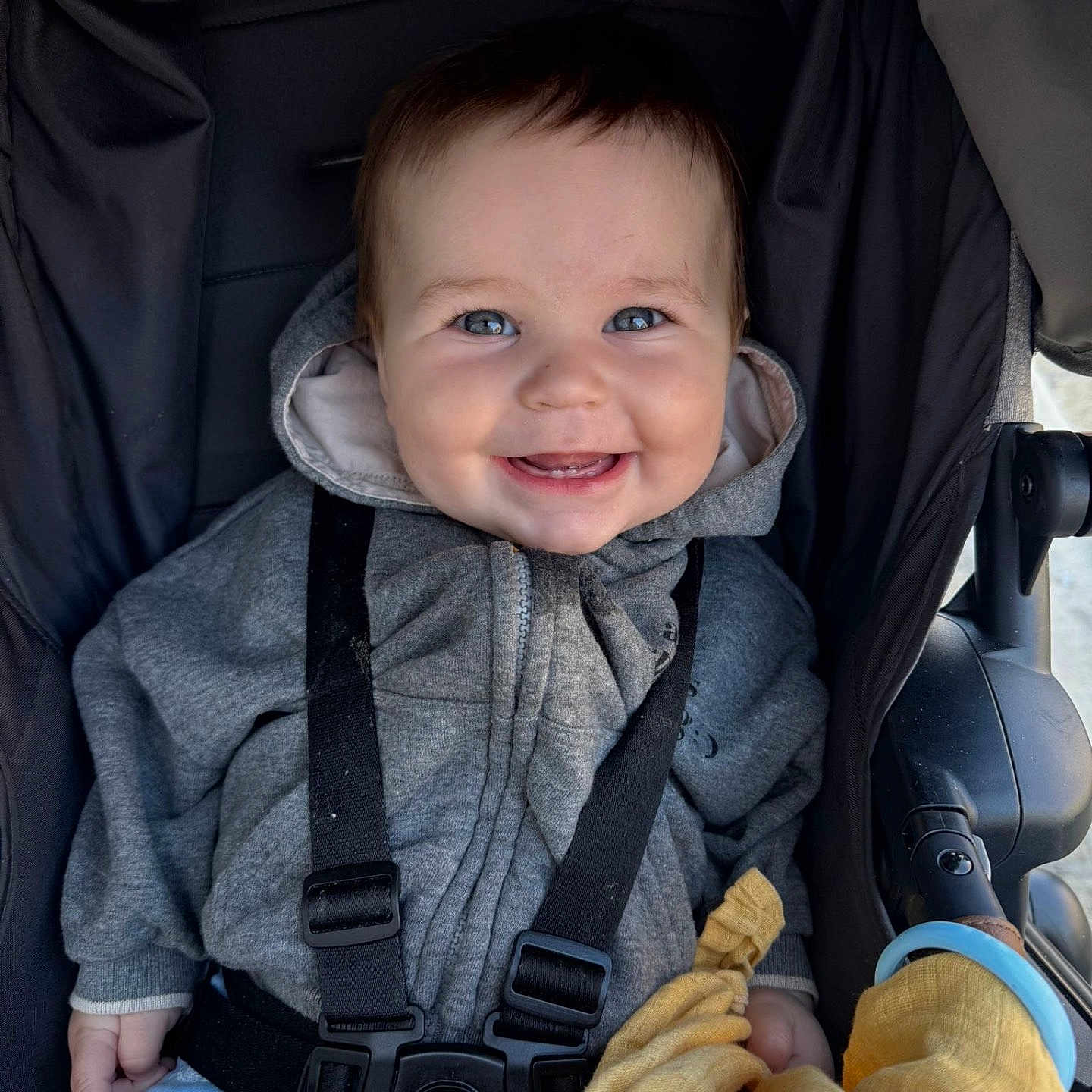 Grayson is registered to the contest to win money with this photo: baby, baby_clothes, black_straps, blue_eyes, child, closeup, clothing, cute, daylight, face, happy, hoodie, infant, joyful, outdoor, person, seated, smiling, stroller, yellow_blanket