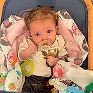 Guinevere joined the competition — help win amazing prizes! baby, pacifier, blanket, toy, curly_hair, blue_eyes, infant, clothing, cushion, fabric, person, cute, indoor, soft_toys, child, baby_girl, playpen, wrapped, portrait, fist