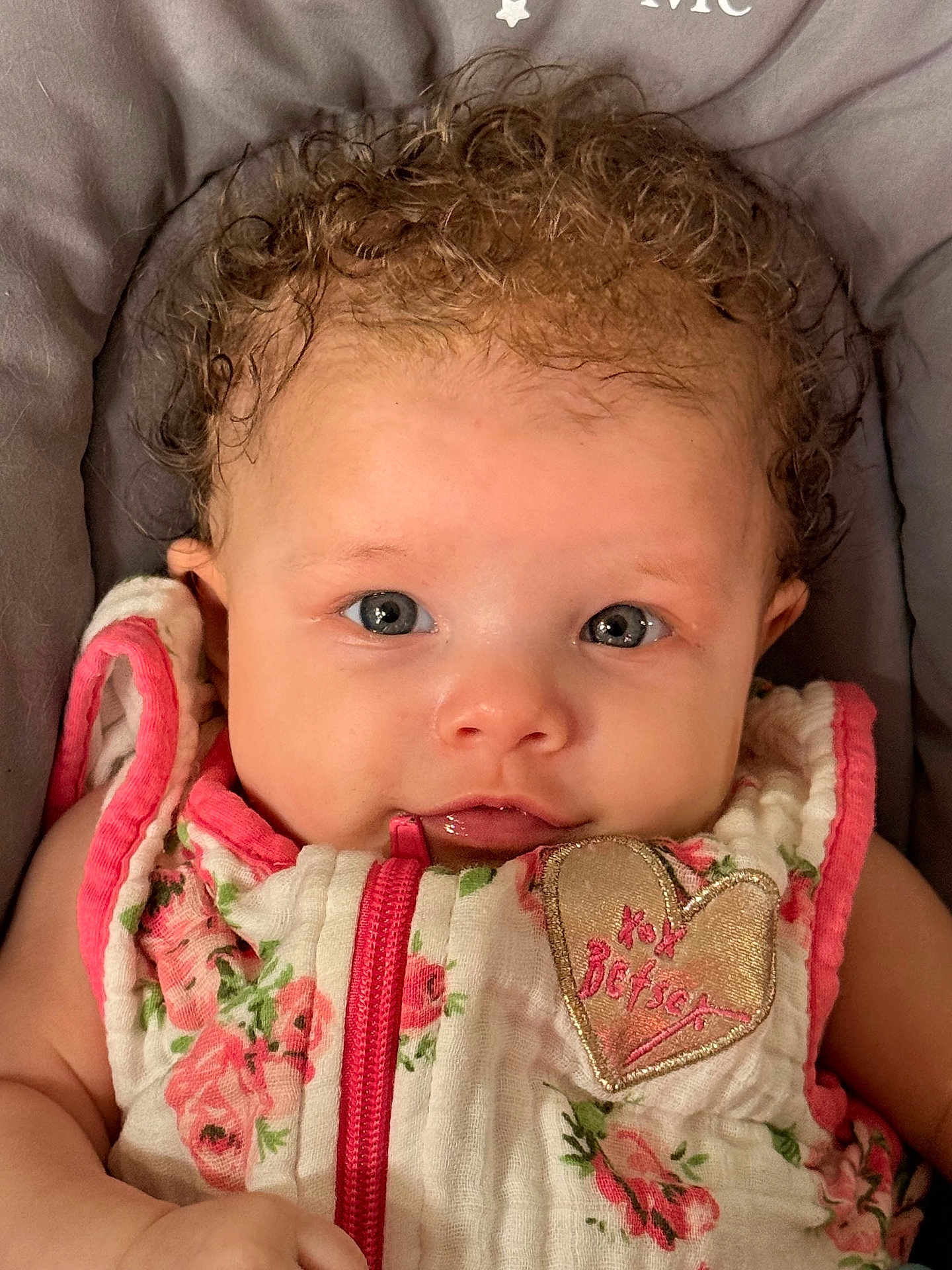 Guinevere joined the competition — help win amazing prizes! baby, infant, curly_hair, blue_eyes, floral_outfit, heart_patch, cute, close_up, portrait, child, soft_cushion, pink, white, fabric, clothing, young, person, lying_down, apparel, adorable