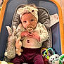 Guinevere is registered to the contest to win money with this photo: baby, pacifier, headband, baby_chair, toy, stuffed_animal, plush_toy, colorful_rings, purple_pants, white_shirt, curly_hair, wooden_floor, cushion, infant, child, cute, indoors, portrait, seated, playtime