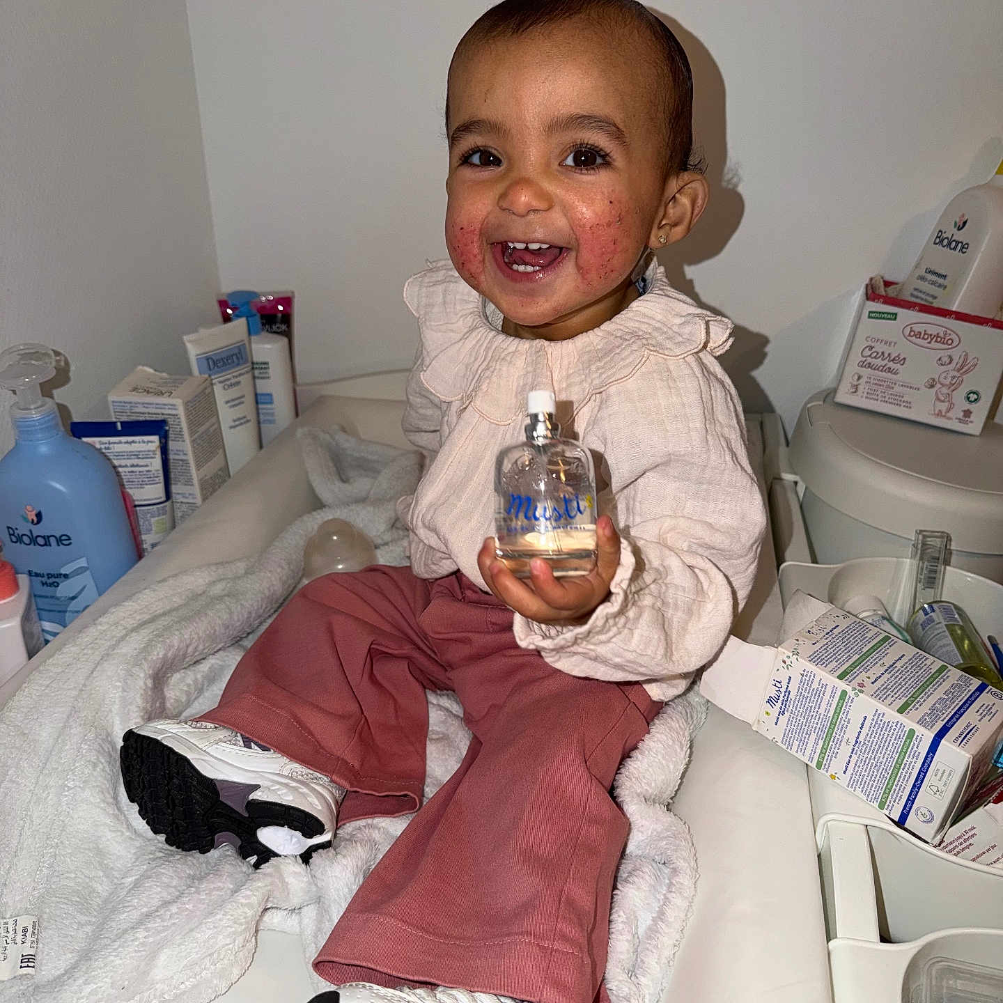 Layanah a rejoint le concours — aidez-le/la à gagner de superbes lots ! baby_care, baby_products, bottle, child, cozy, cute, face, happy, indoor, joyful, long_sleeve_shirt, person, pink_pants, shoes, sitting, skin_condition, smiling, table, toddler, white_blanket