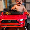 toddler, child, baby, face, smiling, happy, barefoot, toy_car, red_car, ride_on_toy, steering_wheel, vehicle, sports_car, indoor, portrait, sitting, driving, home, blurred_background, photography