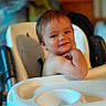 baby, infant, child, high_chair, smiling, portrait, indoor, seated, brown_hair, face, person, baby_tray, furniture, home, photograph, phone_screenshot, gallery_interface, black_border, happy, cute