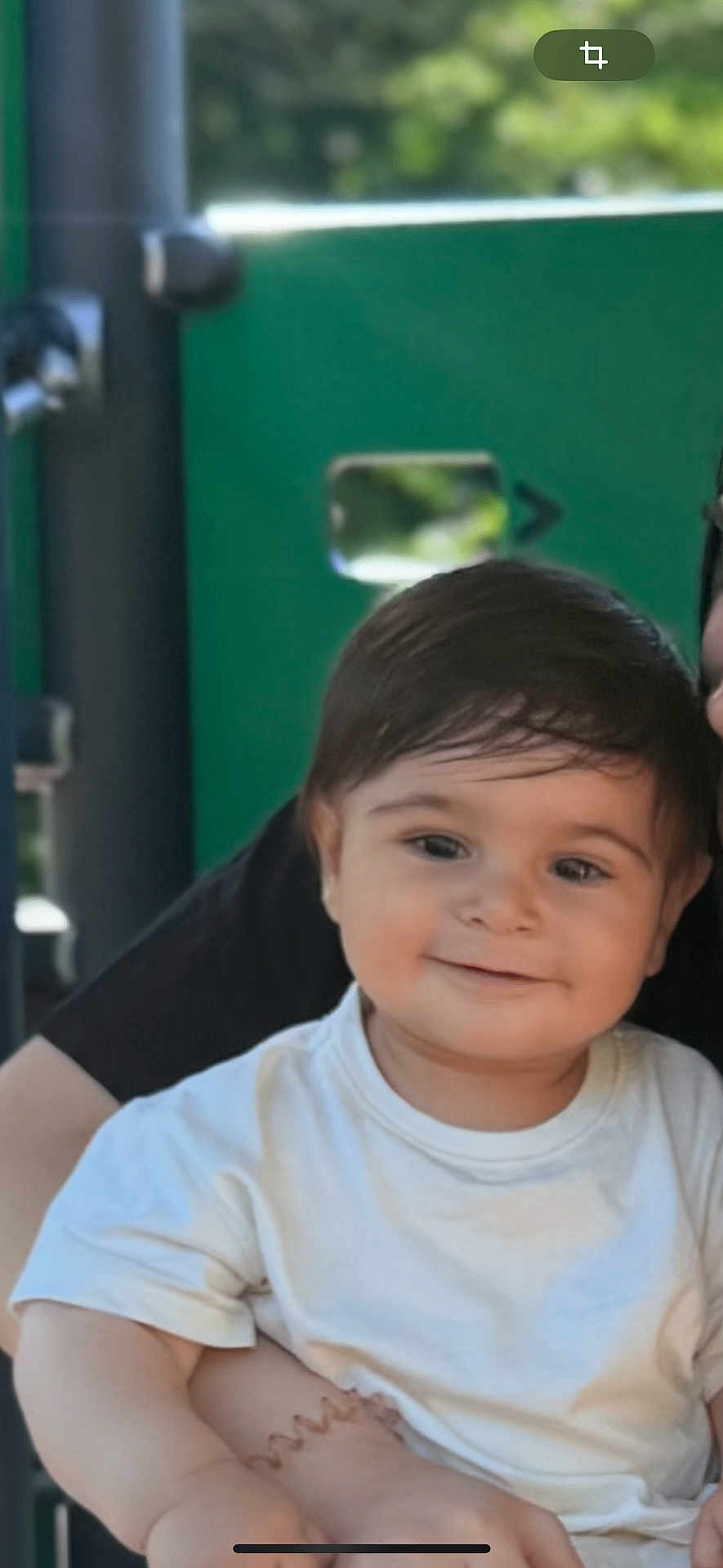 Vigen a rejoint le concours — aidez-le/la à gagner de superbes lots ! toddler, child, smiling, white_shirt, dark_hair, face, portrait, outdoor, playground, adult_arm, holding, happy, person, young_child, casual_clothing, baby, cute, daylight, green_background, blurred_background