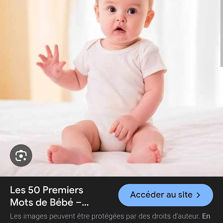 Mekka Lyna a rejoint le concours — aidez-le/la à gagner de superbes lots ! baby, bed, casual, child, curious_expression, cute, early_childhood, hand_raised, human, indoor, infant, light_background, onesie, person, portrait, sitting, small_feet, soft_lighting, white_clothing, young_child