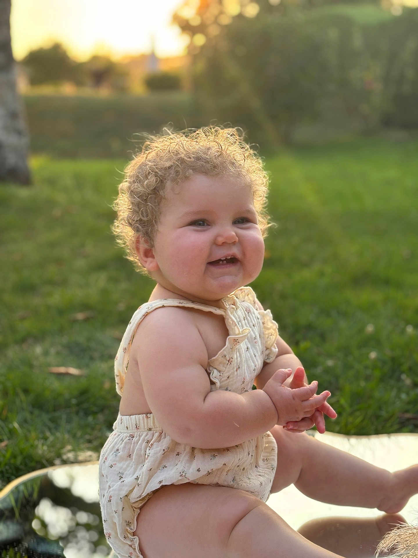 Abygaëlle participe au concours pour gagner de l'argent avec cette photo : baby, child, curly_hair, smiling, clapping_hands, outdoor, grass, sunlight, reflection, cute, happy, summer, nature, portrait, infant, skin, bare_arms, sitting, daytime, warm_light