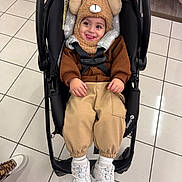 Pierre joined the competition — help win amazing prizes! toddler, child, stroller, baby, hat, bear_hat, brown_clothing, pants, white_sneakers, indoor, floor_tiles, smiling, tongue_out, cute, seatbelt, shopping, clothing_rack, footwear, playful, person