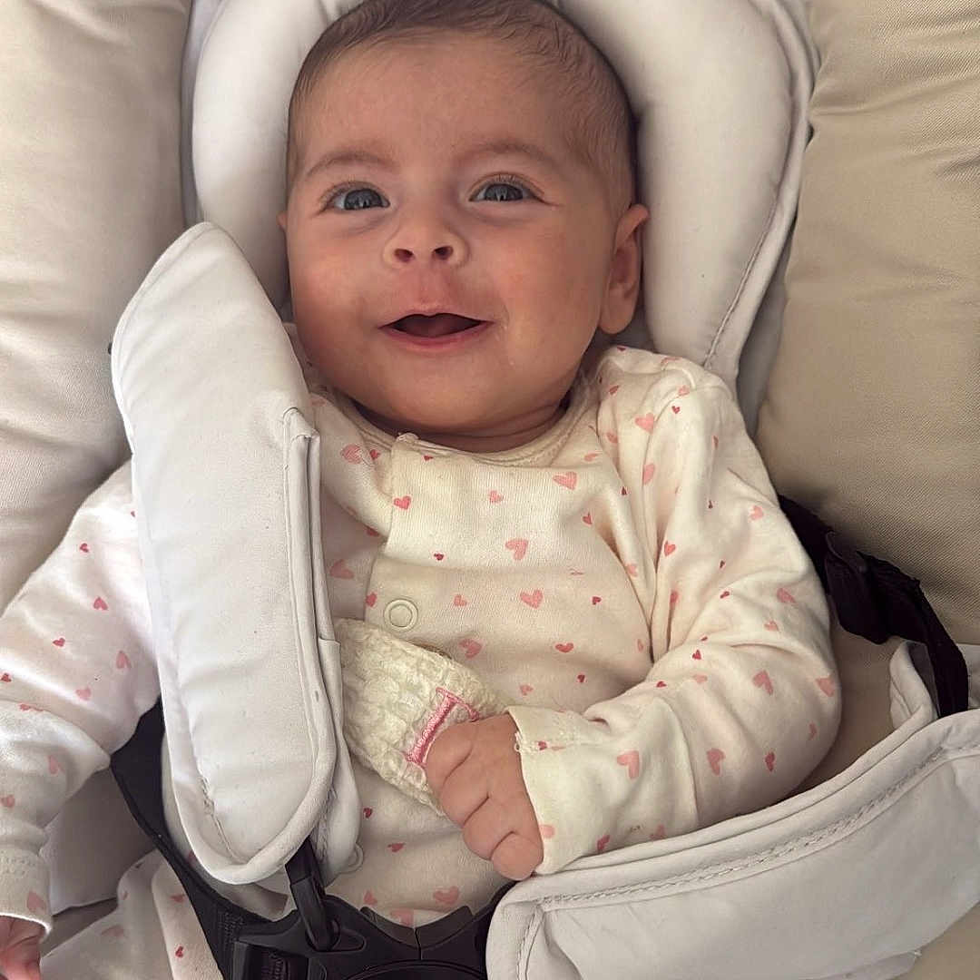 Liv a rejoint le concours — aidez-le/la à gagner de superbes lots ! baby, infant, smile, onesie, heart_pattern, baby_seat, harness, cushion, comfort, child, cute, portrait, happy, indoor, clothing, person, face, seatbelt, straps, young