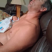 Chaos is registered to the contest to win money with this photo: adult, baby, blanket, couch, family, furniture, home, indoor, interior, lamp, living_room, man, newborn, peaceful, person, portrait, relaxing, resting, shirtless, sleeping