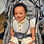 Landon is registered to the contest to win money with this photo: baby, child, clothing, curly_hair, cute, floor, happiness, happy, indoors, infant, playful, portrait, romper, seatbelt, secured, sitting, smiling, stroller, wooden_floor, young_child
