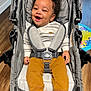 baby, baby_boy, baby_girl, bear_slippers, casual_wear, child, cozy_clothing, curly_hair, cute, happy, indoor, infant, playmat, portrait, real_photo, seated, smiling, strapped_in, stroller, wooden_floor
