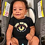 baby, smiling, curly_hair, car_seat, onesie, pacifier, black_clothing, infant, child, cute, happy, sitting, indoor, person, young_child, seat, clothing, skin, portrait, baby_smile