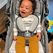 Landon joined the competition — help win amazing prizes! baby, baby_clothing, child, curly_hair, cute, fuzzy_socks, happy, home, indoor, infant, mustard_pants, person, playmat, portrait, seatbelt, sitting, smiling, striped_shirt, stroller, wood_floor