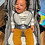 Landon is registered to the contest to win money with this photo: baby, baby_gear, black_socks, child, clothing, curly_hair, cute, footwear, happy, indoor, infant, mustard_pants, person, plush_slippers, seatbelt, smiling, striped_sweater, stroller, toy, wooden_floor