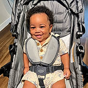 Landon joined the competition — help win amazing prizes! baby, buttoned_shirt, casual_wear, child, clothing, curly_hair, cute, happy, indoor, infant, person, playful, portrait, safety_harness, seat, seated, smiling, stroller, wooden_floor, young_child
