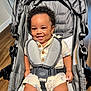 baby, buttoned_shirt, casual_wear, child, clothing, curly_hair, cute, happy, indoor, infant, person, playful, portrait, safety_harness, seat, seated, smiling, stroller, wooden_floor, young_child